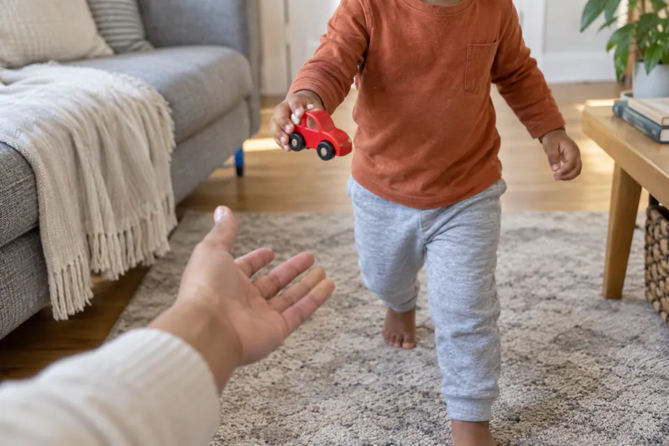 A child bringing a red toy car to an adult during a color hunt.