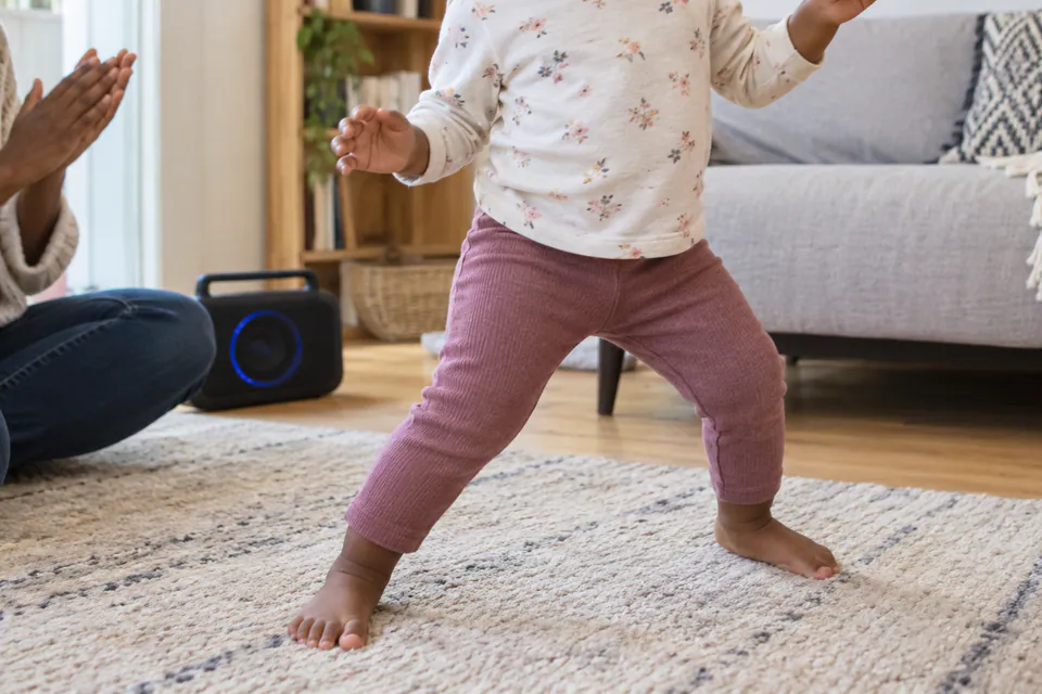 A child dancing beside an adult and a small speaker.