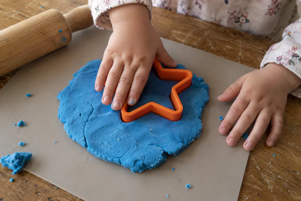 A child pressing a star-shaped cutter into blue playdough.