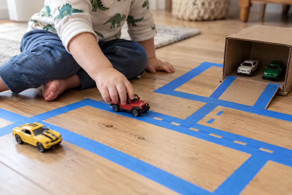 A child driving toy cars along roads made from painter's tape.