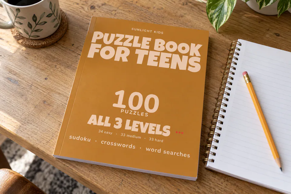 The orange Puzzle Book for Teens cover beside a notebook and pencil.