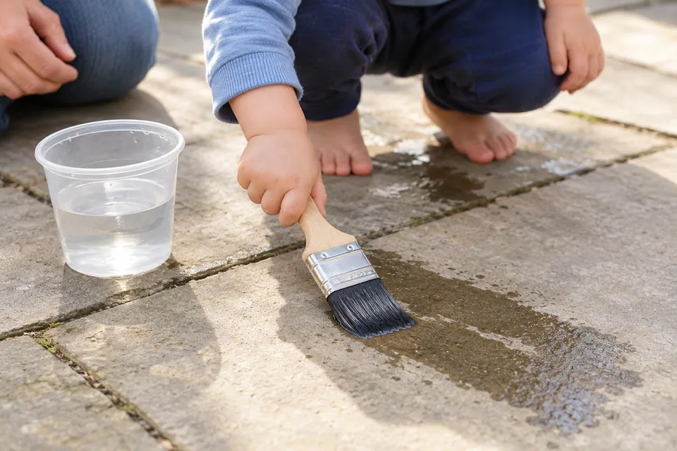 A toddler painting patio paving stones with a brush and plain water.