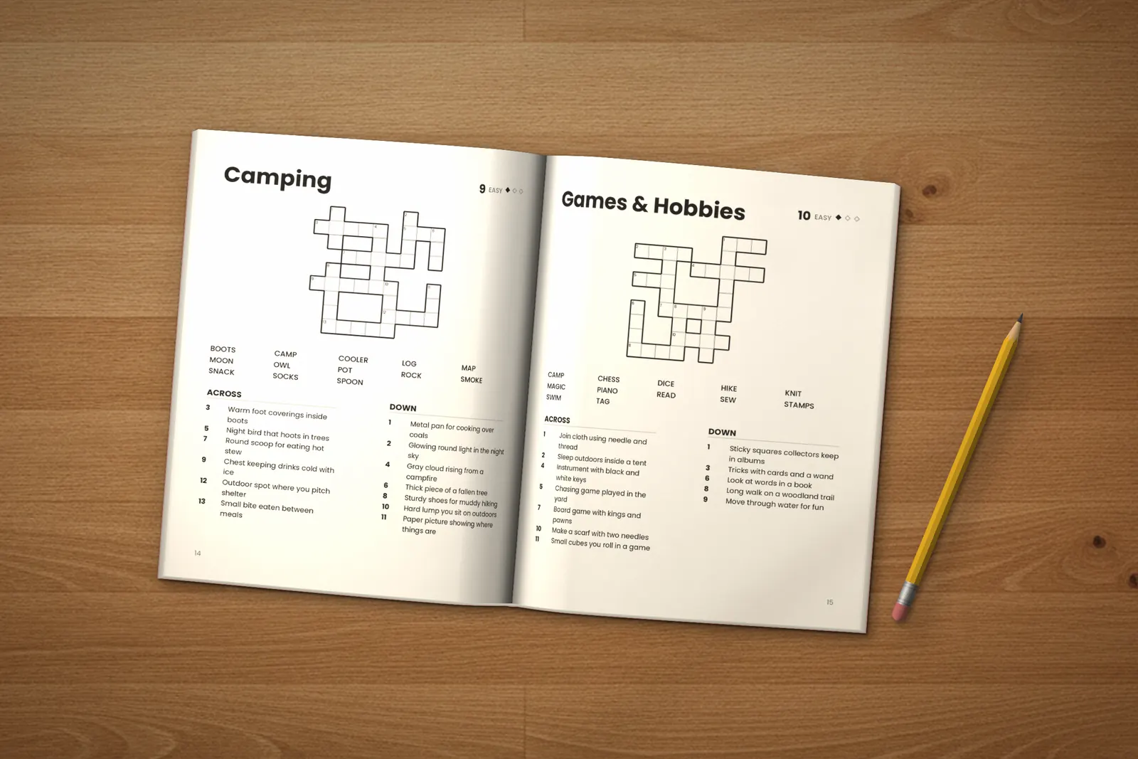 Crossword Puzzles for Kids: Easy lying open on a wooden table, showing two crosswords (“Camping” and “Games & Hobbies”), next to a yellow pencil