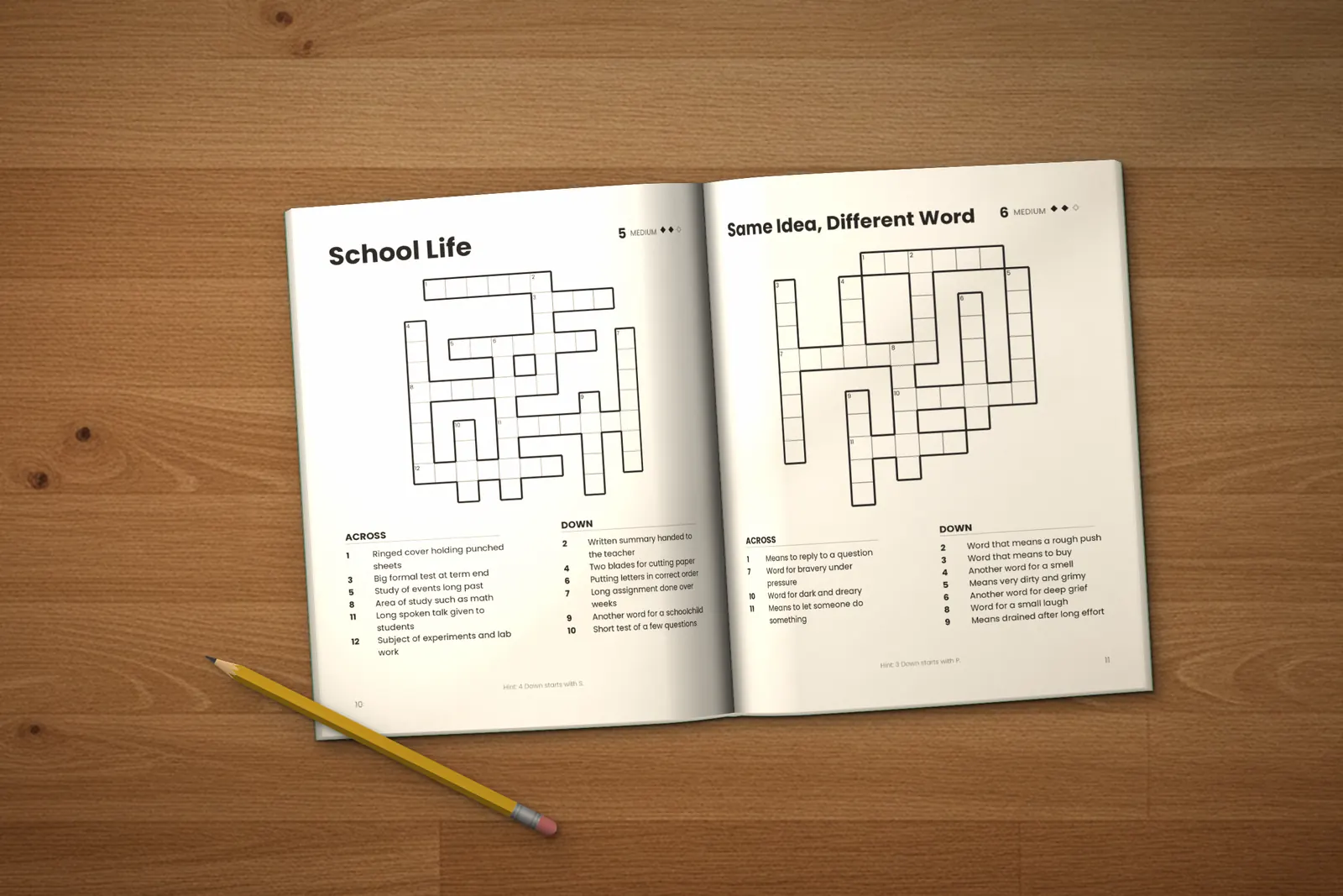 Crossword Puzzles for Kids: Medium lying open on a wooden table, showing two crosswords (“School Life” and “Same Idea, Different Word”), next to a yellow pencil