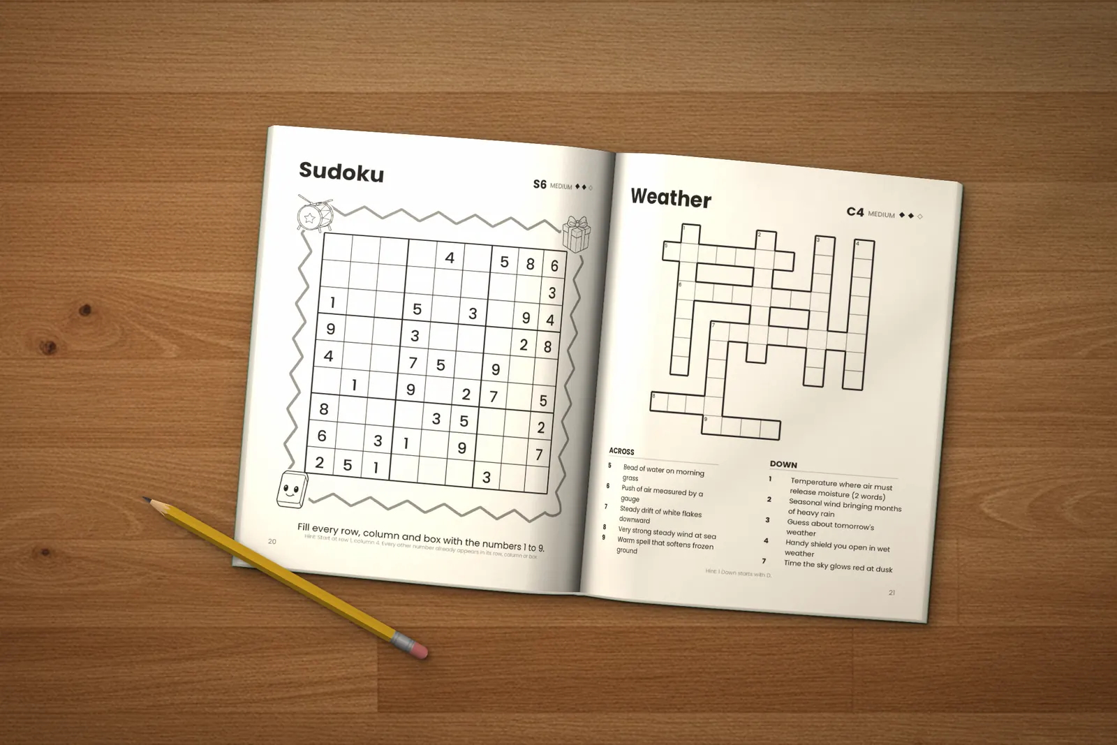 Puzzle Book for Kids: Medium lying open on a wooden table, showing a medium sudoku and the “Weather” crossword, next to a yellow pencil